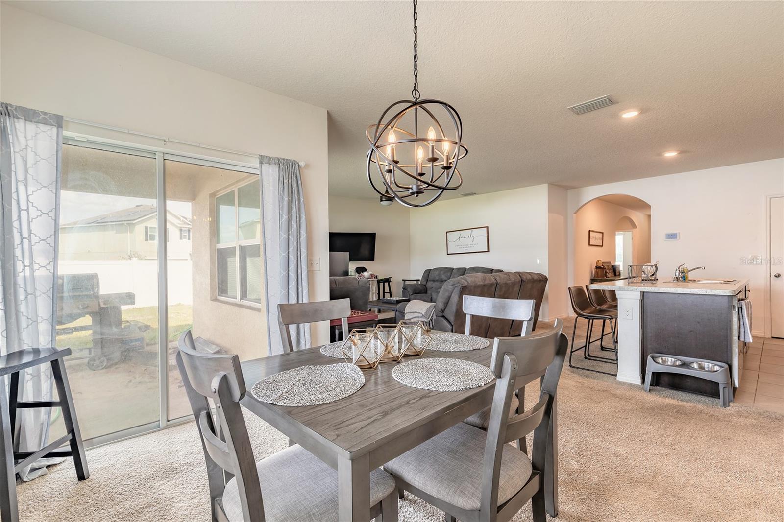 Open-plan dining and living area with a gray sectional, kitchen island, and sliding glass patio doors.