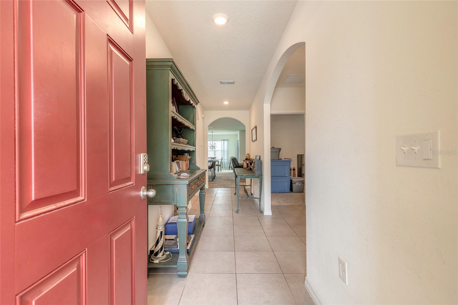 Entryway with an open red front door, tiled floor, green console cabinet, and arched hallways.