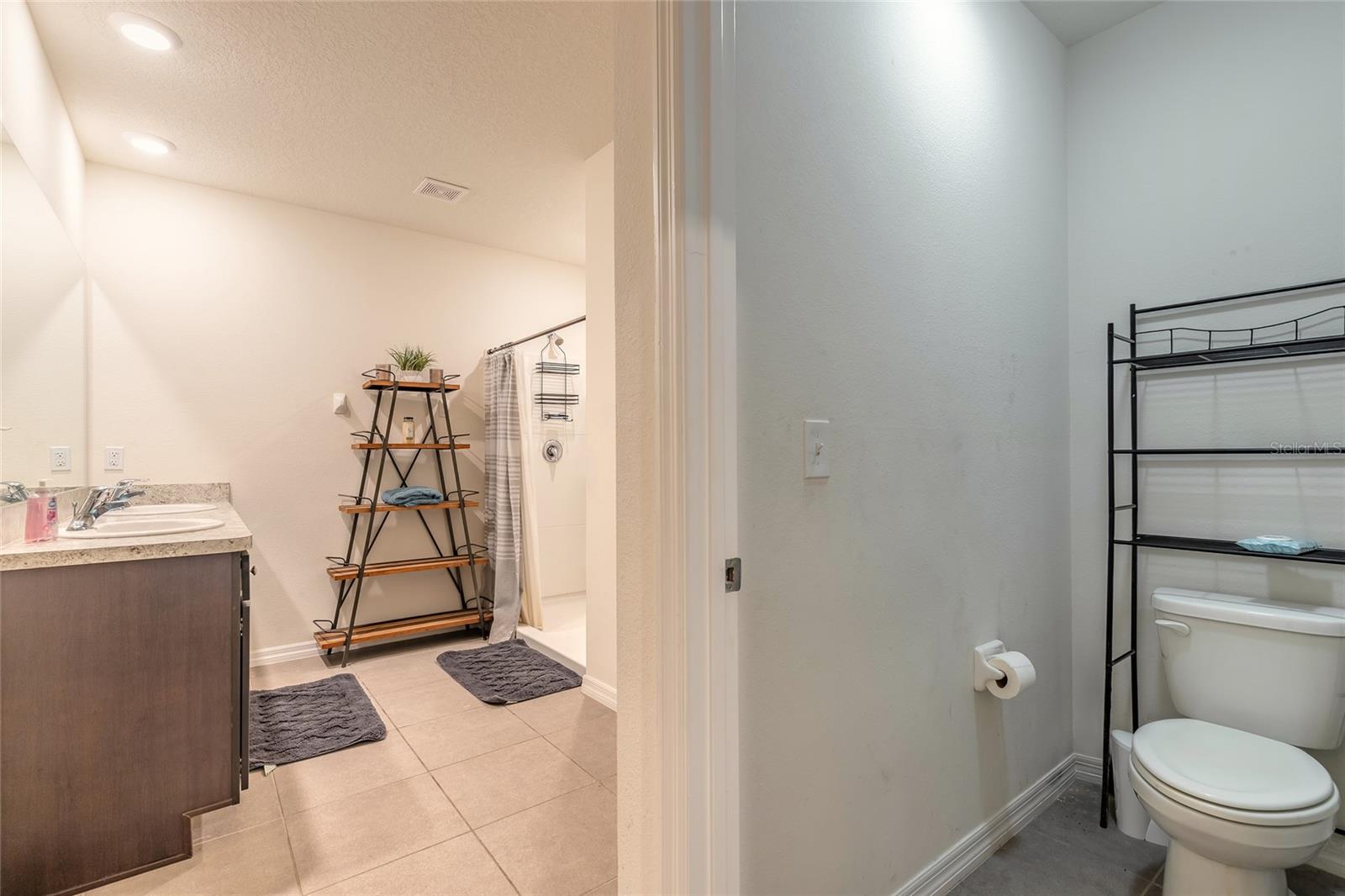 Bathroom with a dark wood vanity, tiled floor, shower, and separate toilet area.
