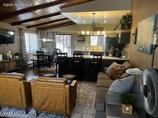Open-plan living and dining area with exposed wood beams, leather armchairs, and a gray sofa.