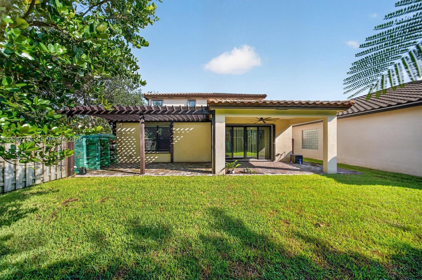 Home’s rear patio with a dark pergola, sliding glass doors, and a broad green lawn.