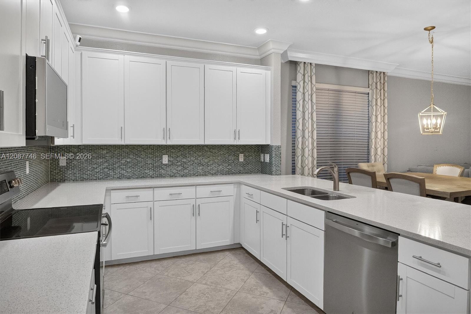 Modern kitchen with white cabinets, dark mosaic backsplash, peninsula sink, and dining area.
