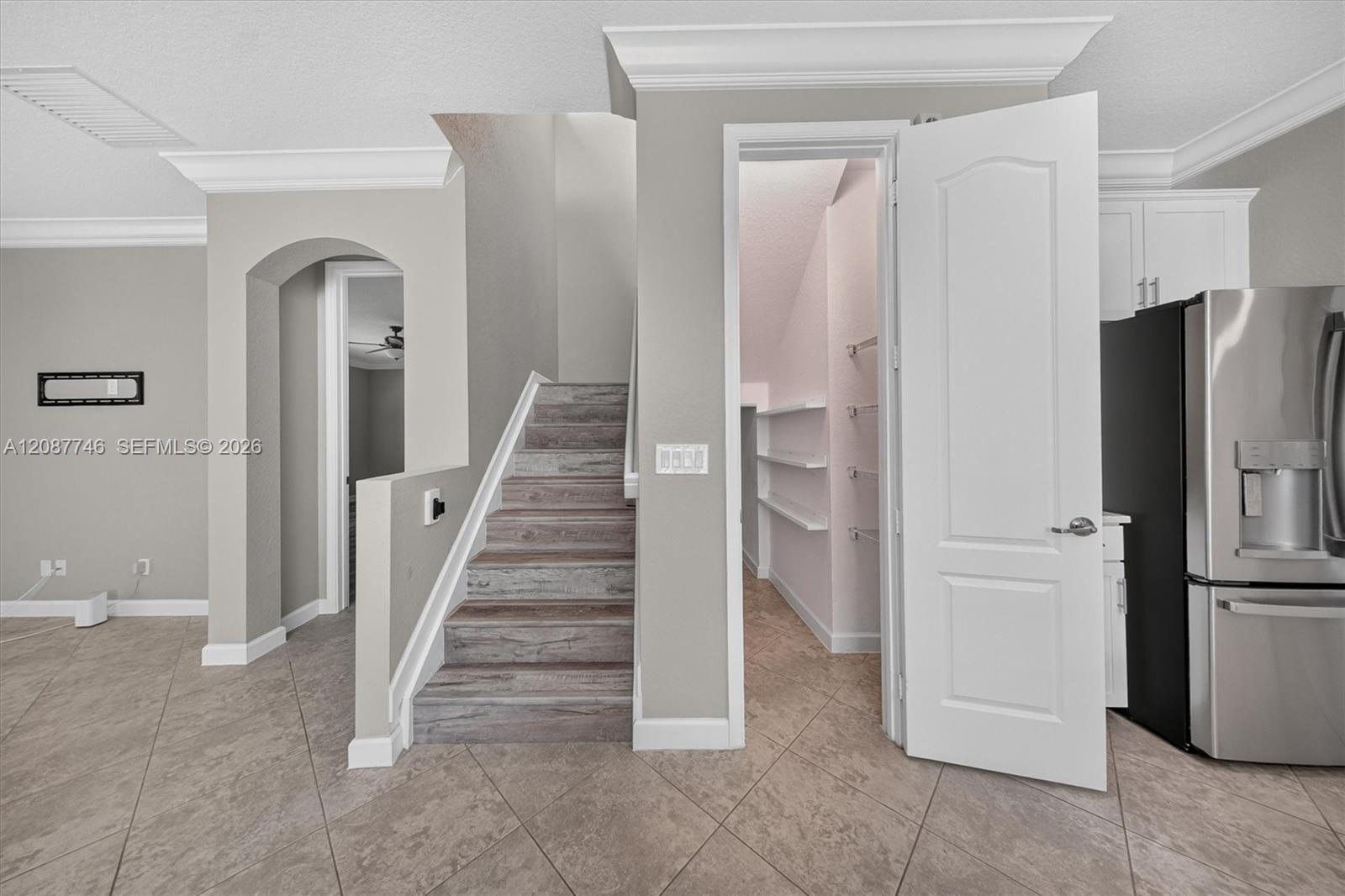 Staircase with wood-look steps beside an open storage closet and stainless steel refrigerator.