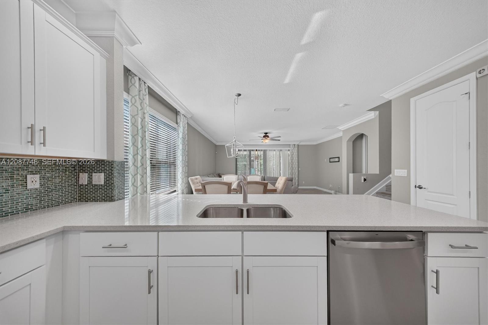 Kitchen with white shaker cabinets, mosaic tile backsplash, and a wide counter opening to the dining area.