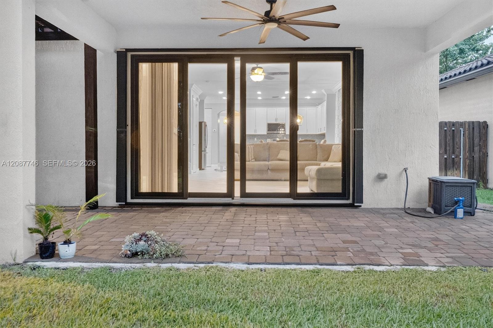 Covered paver patio with ceiling fan and sliding doors opening to a furnished living room.