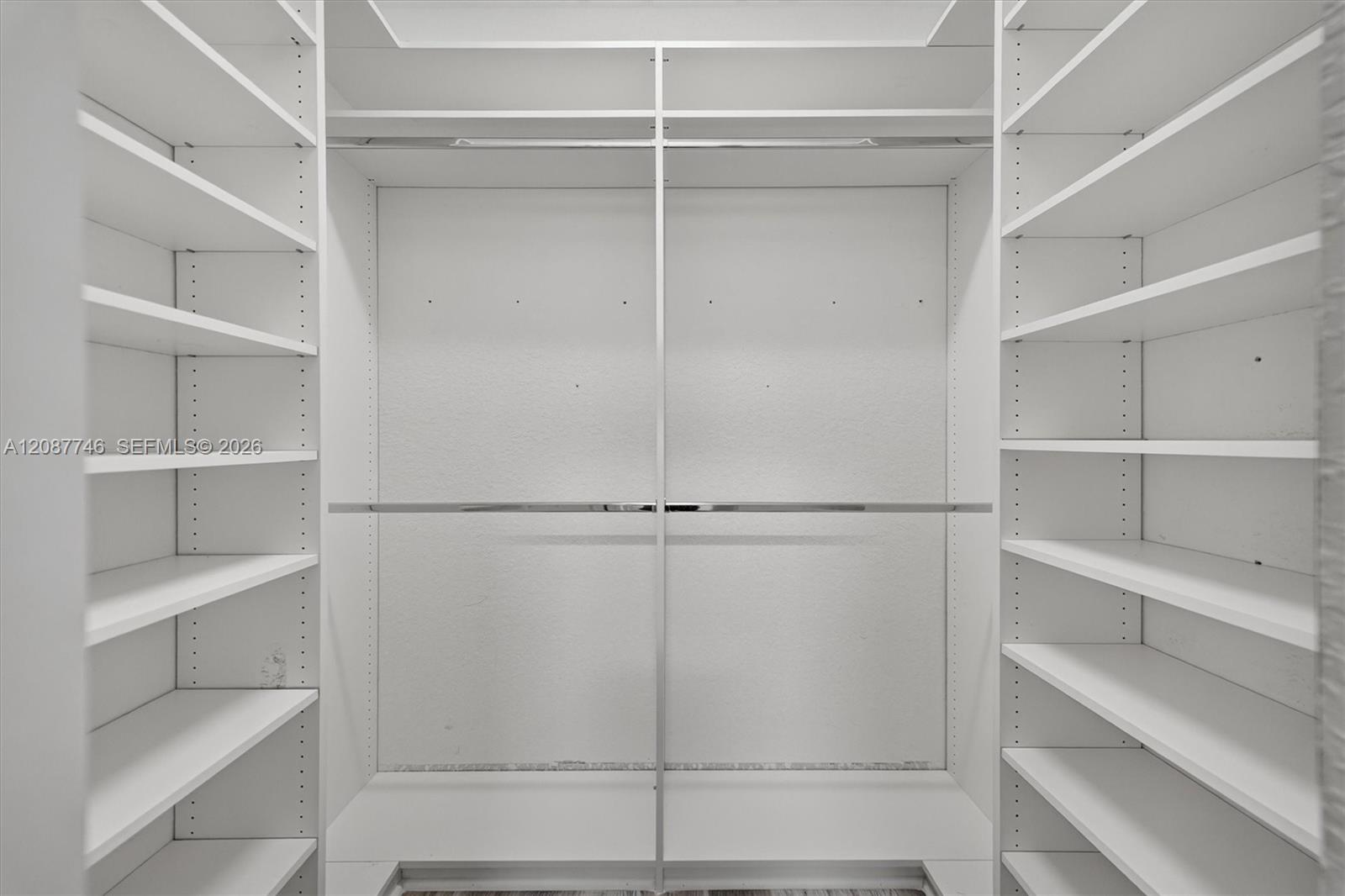 Walk-in closet with white built-in shelving and hanging rods across the back wall.