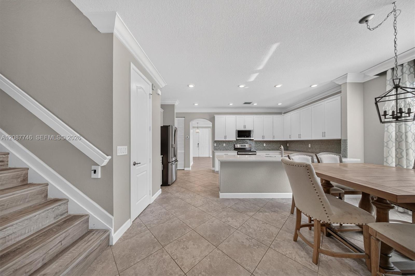 Open-plan kitchen and dining area with white cabinetry, a central island, and a staircase.