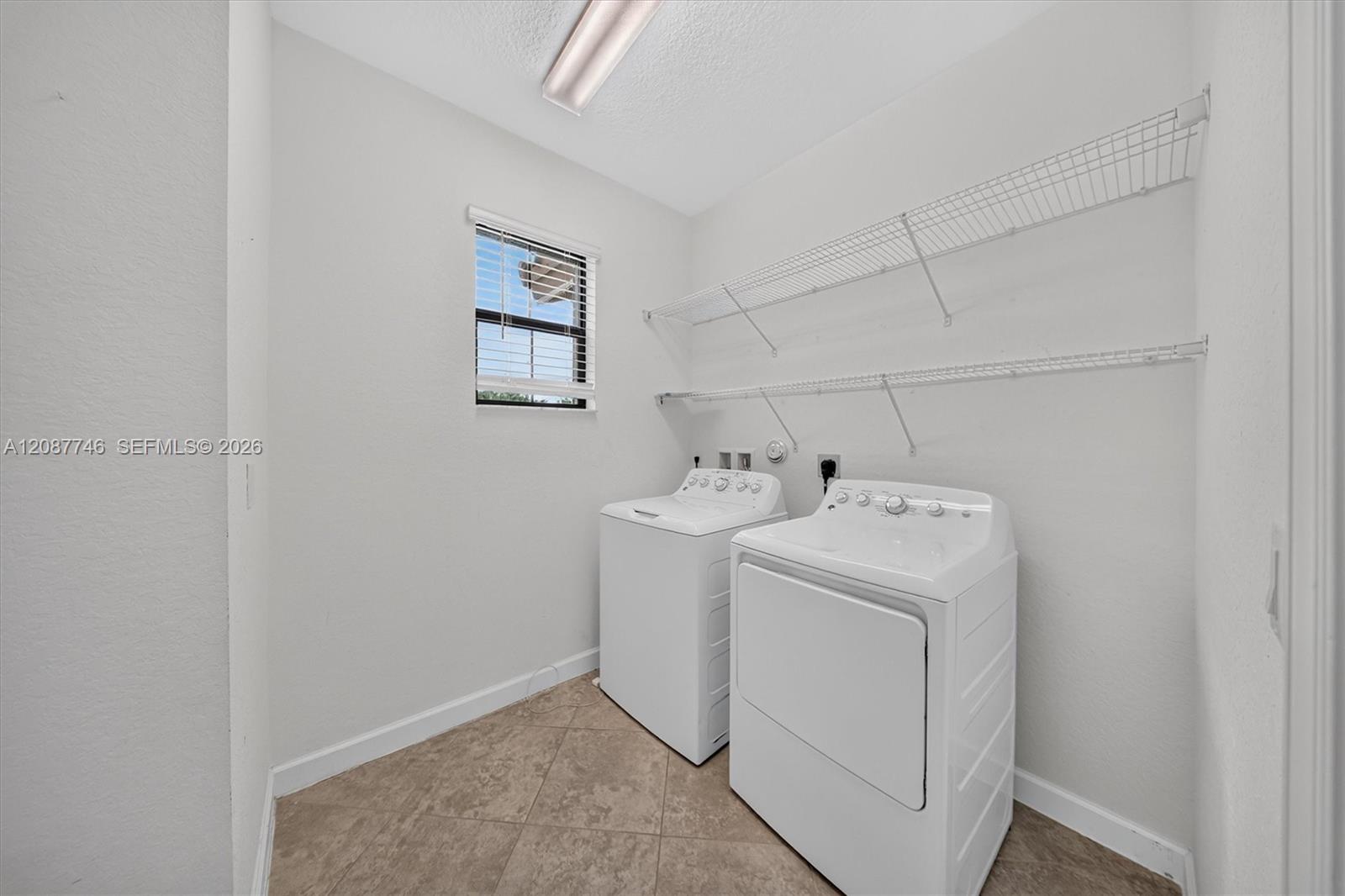 Laundry room with a white washer and dryer, wire shelving, and a small window.