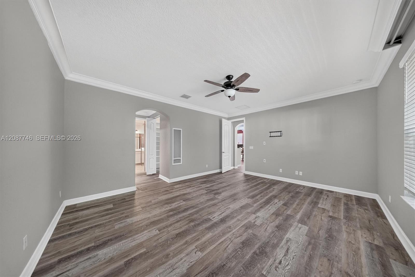 Empty room with gray walls, wood-look flooring, a ceiling fan, and a window with blinds.