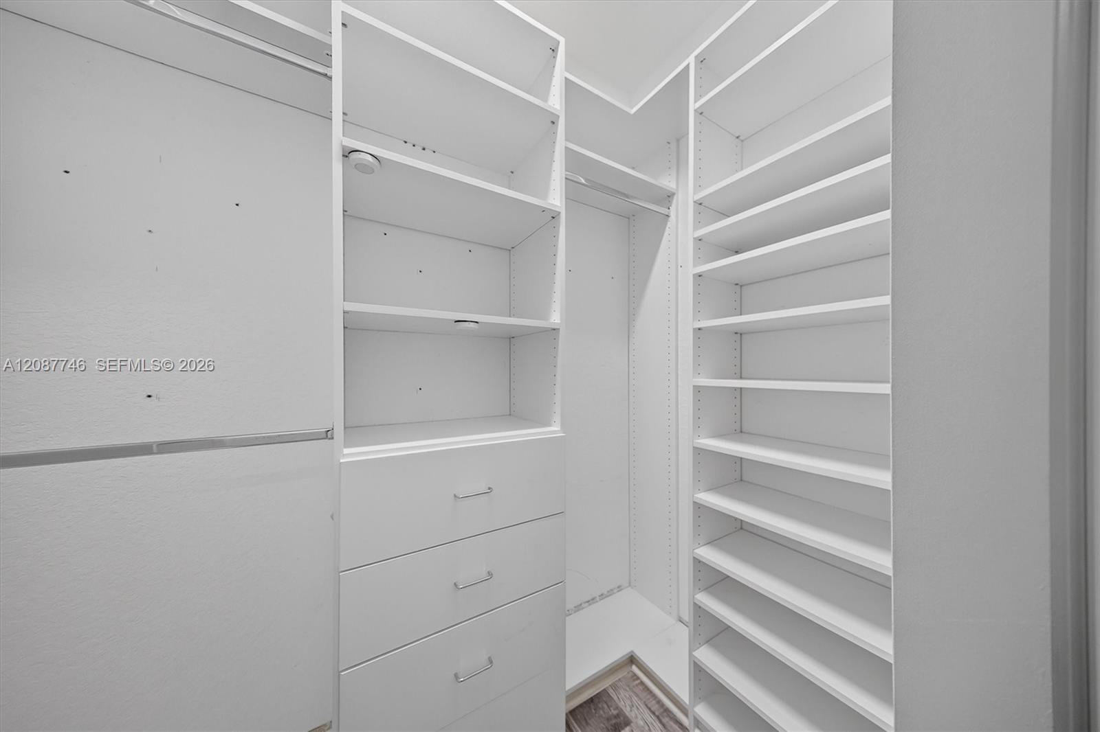Walk-in closet with built-in white shelves, hanging rails, and drawers.