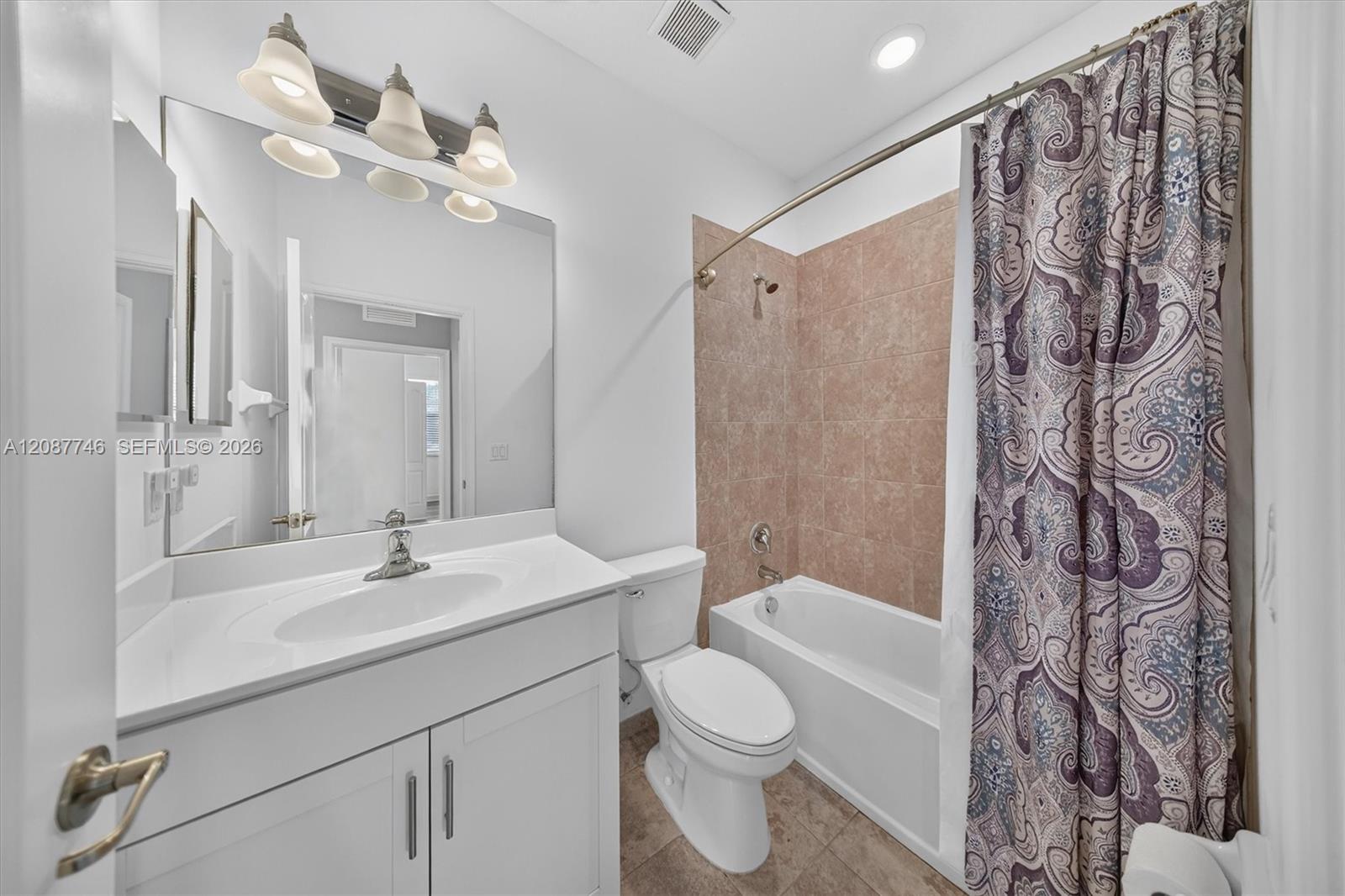 Bathroom with white vanity, toilet, and bathtub behind a patterned shower curtain.