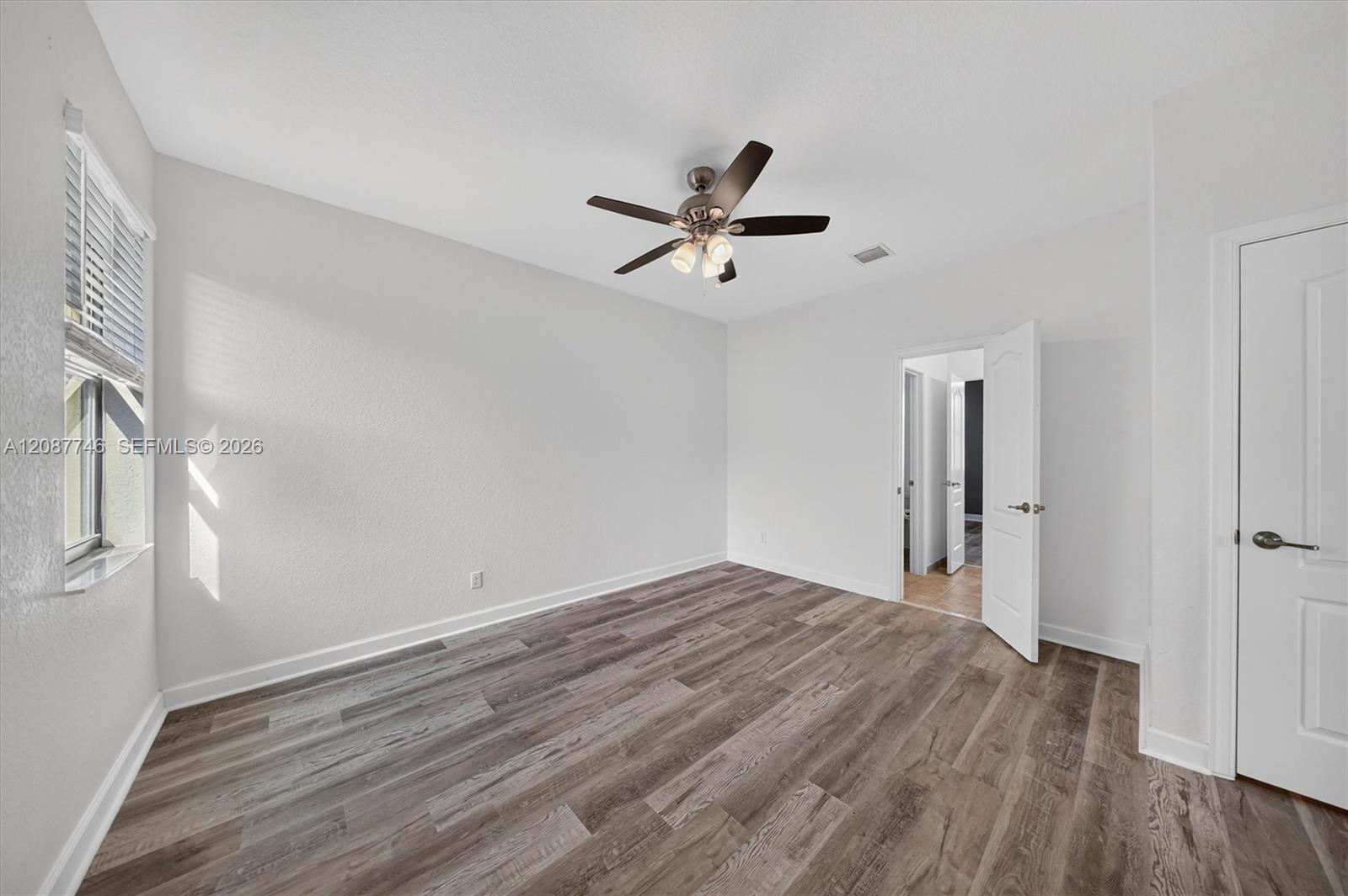 Vacant bedroom with wood-look flooring, a ceiling fan, and a sunlit shuttered window.