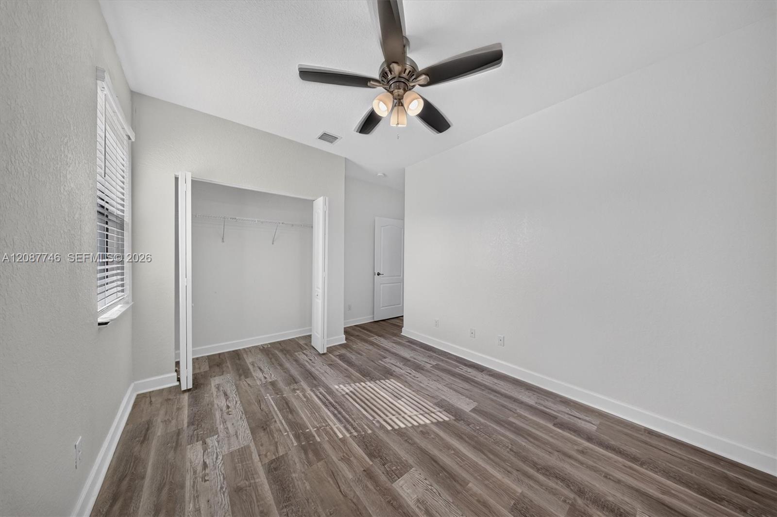 Unfurnished bedroom with gray plank flooring, an open closet, window blinds, and a ceiling fan.