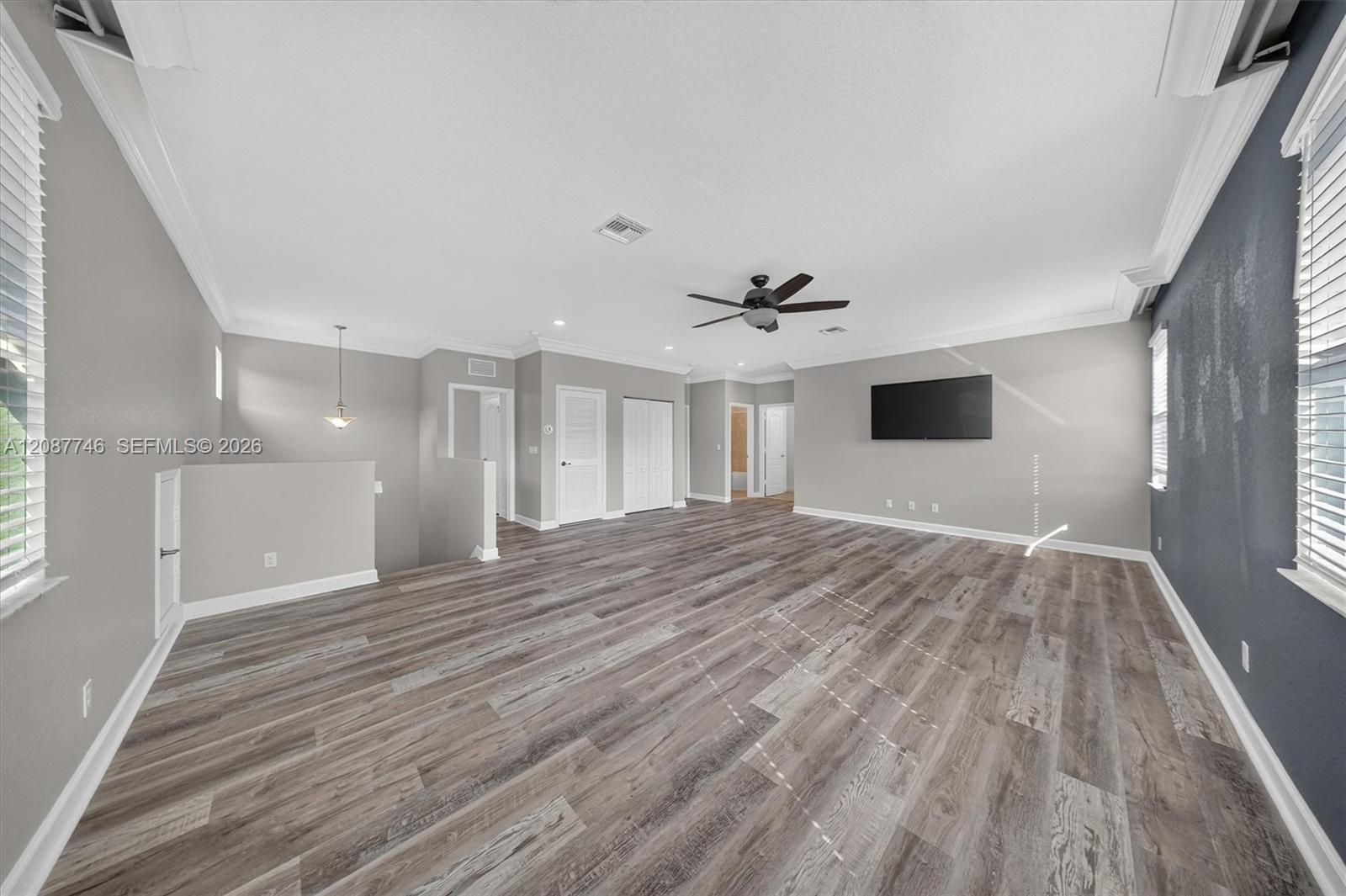 Empty living room with gray wood-look floors, ceiling fan, and wall-mounted television.