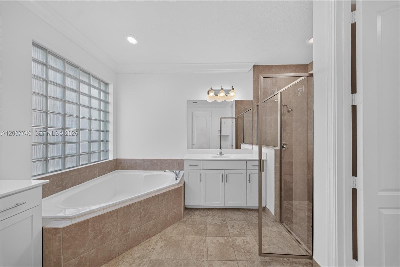 Spacious bathroom with a soaking tub beneath a glass-block window and a glass-enclosed shower.