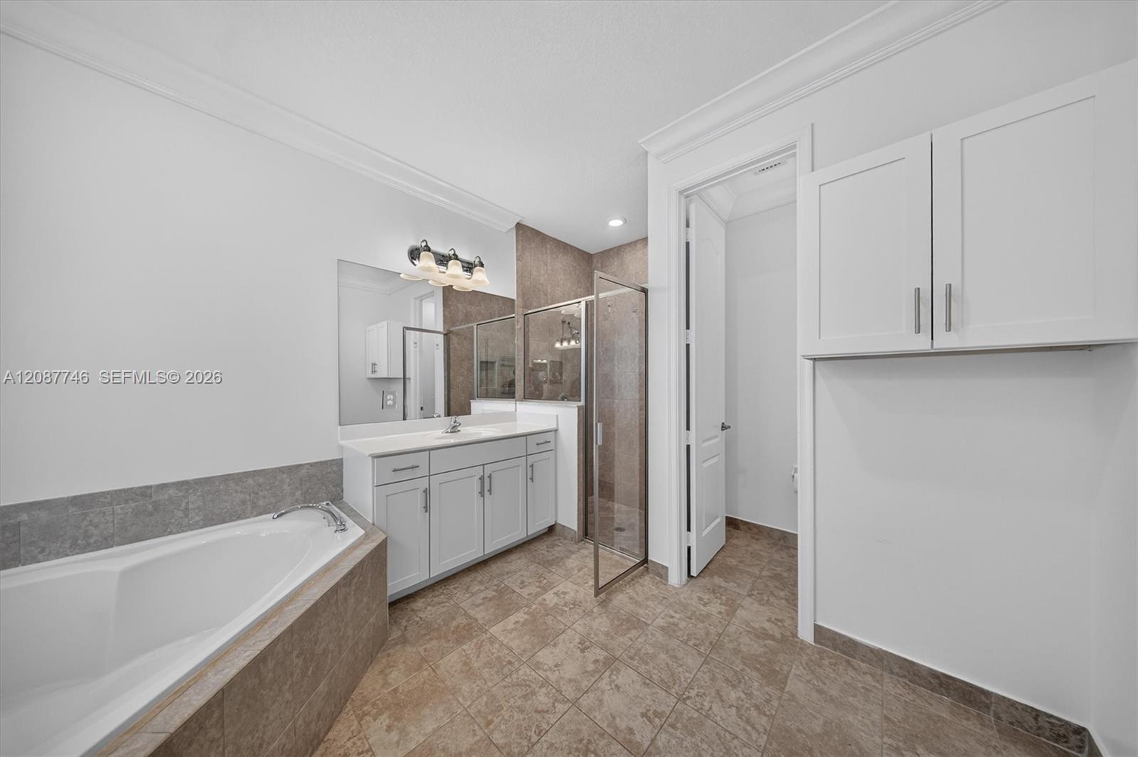 Bathroom with a soaking tub, glass shower, white vanity, and tan tile.