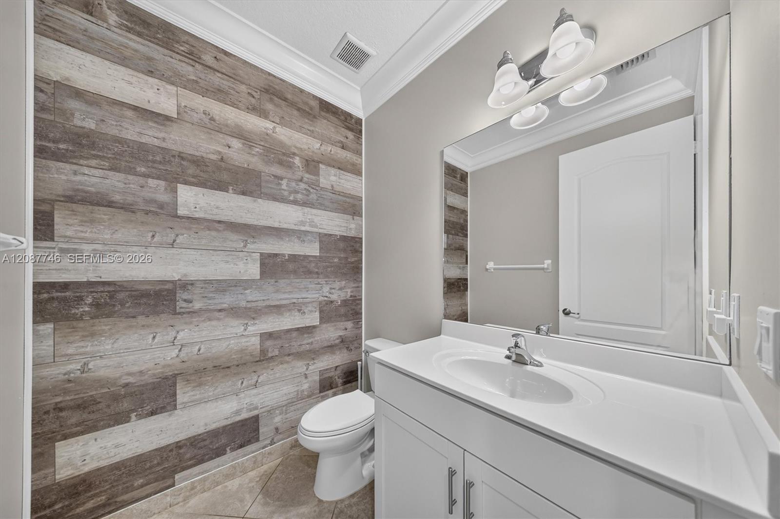 Bathroom with a white vanity and mirror beside a wall of rustic wood-look tile.
