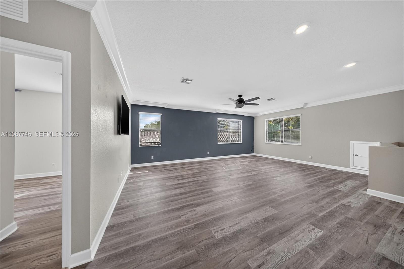 Unfurnished living room with gray plank flooring, a dark accent wall, several windows, and a ceiling fan.