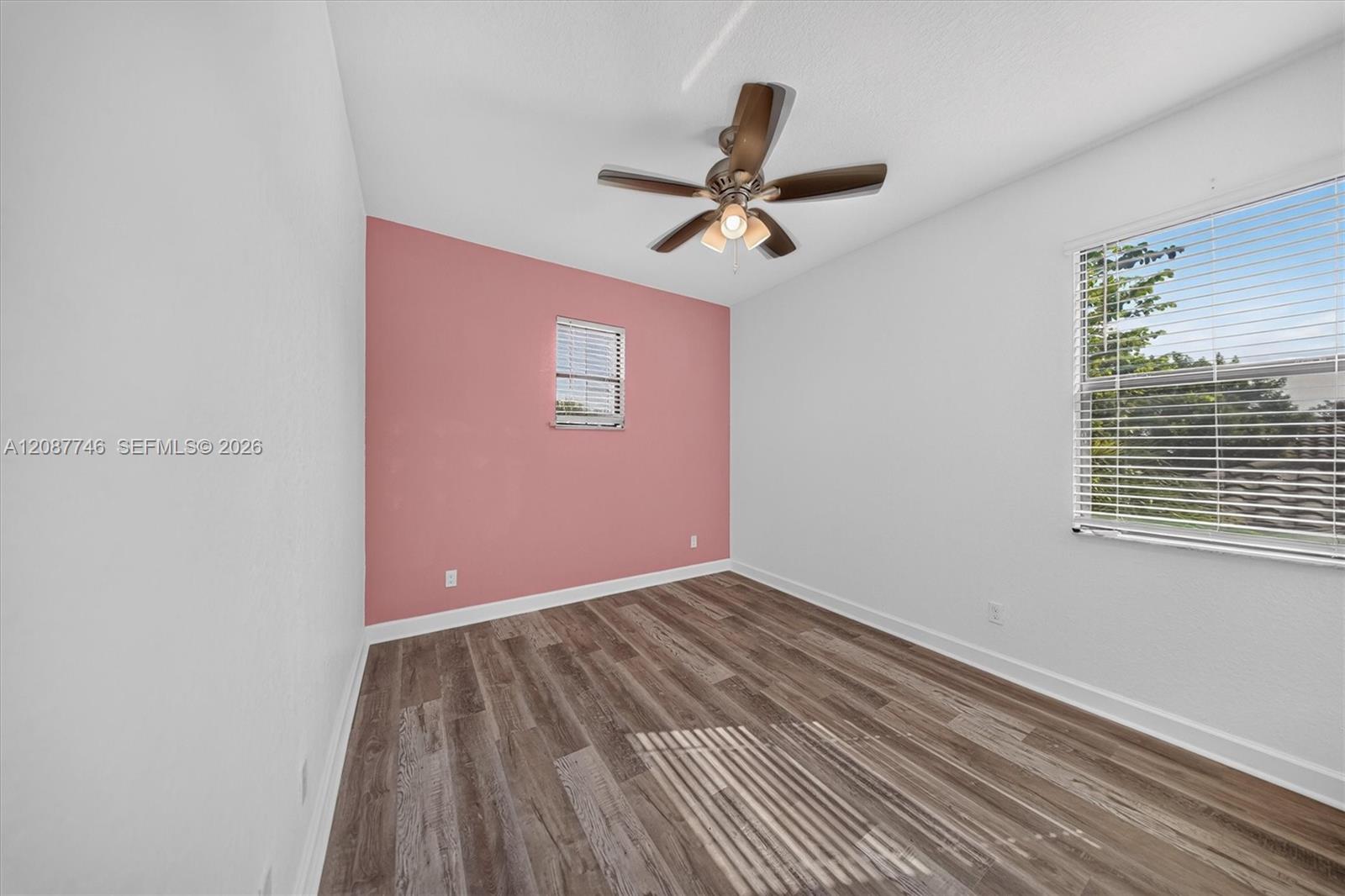 Empty bedroom with wood-look flooring, a dusty pink accent wall, and a ceiling fan.