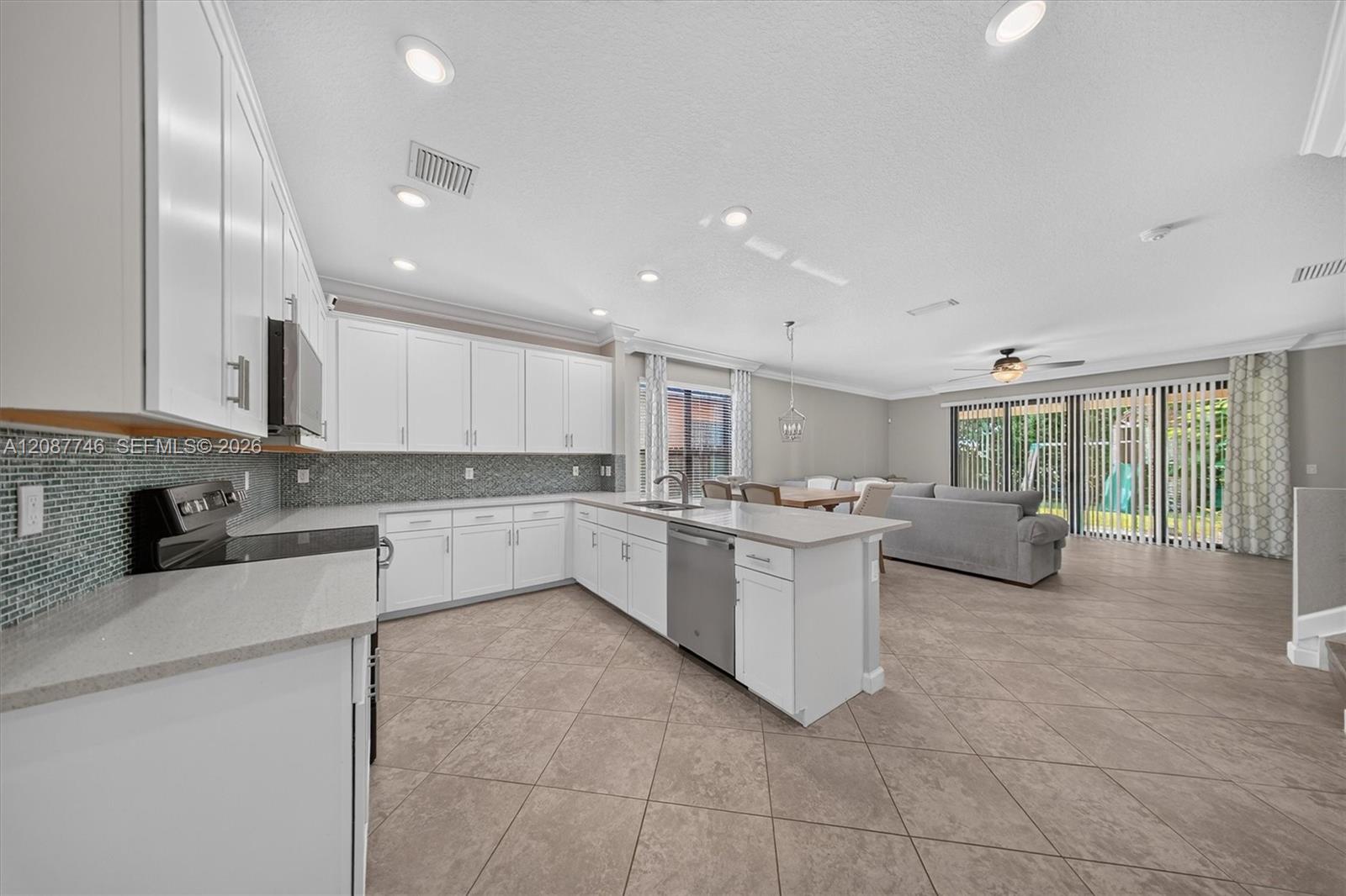 Open-plan kitchen with white cabinets and a large island adjoining a furnished living area.