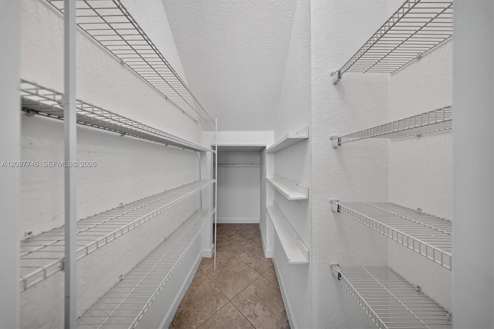 Walk-in closet with wire shelving on both sides and a brown tile floor.