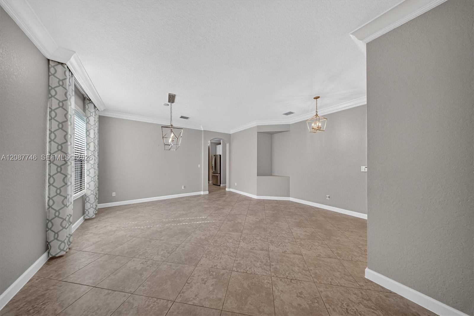 Empty dining room with large tile flooring, two pendant lights, and patterned curtains.