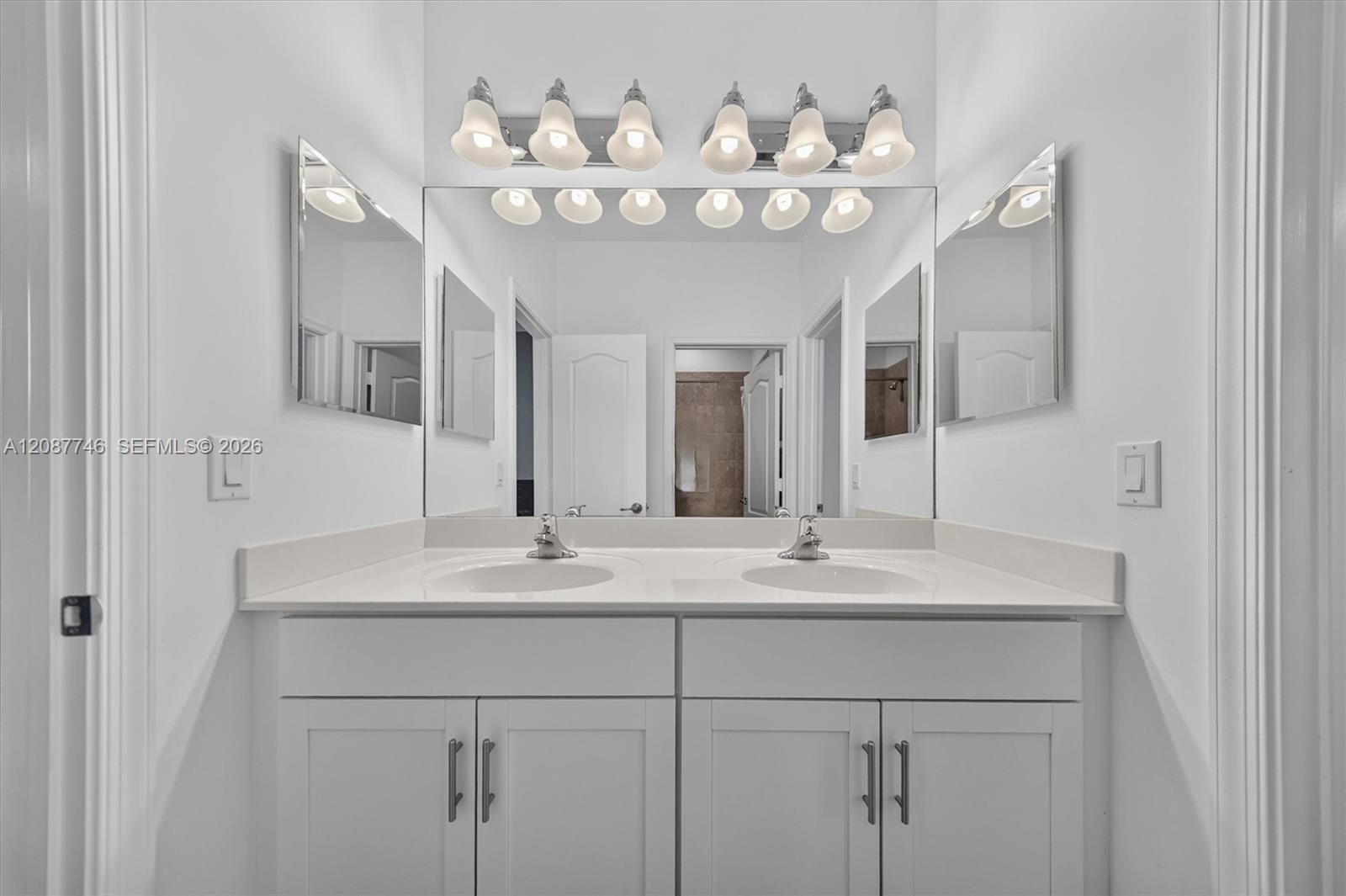 Bathroom double vanity with white cabinetry, two sinks, mirrored walls, and vanity lights.