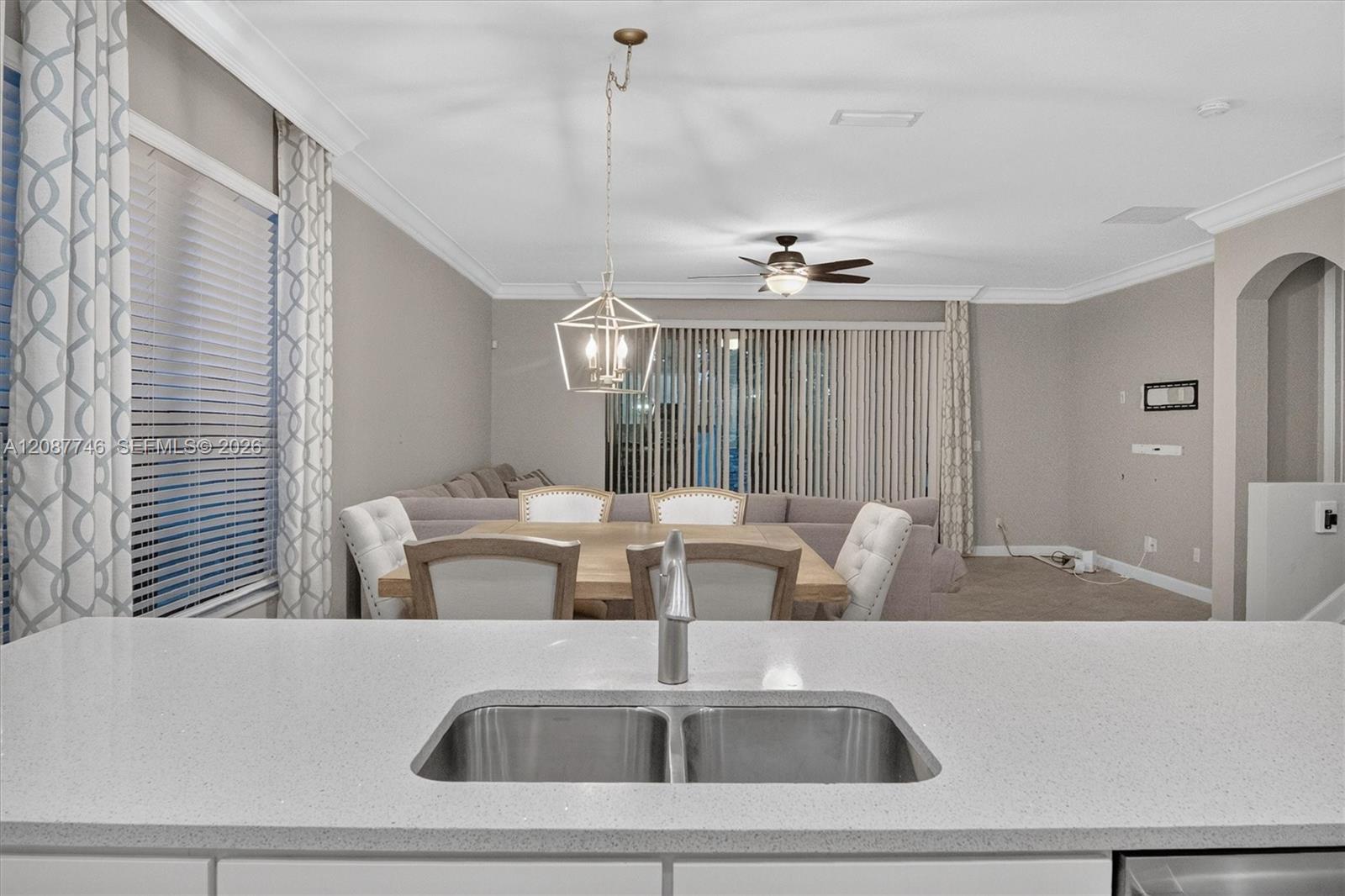 Dining and living area viewed over a kitchen sink, with a table, upholstered chairs, and sectional sofa.