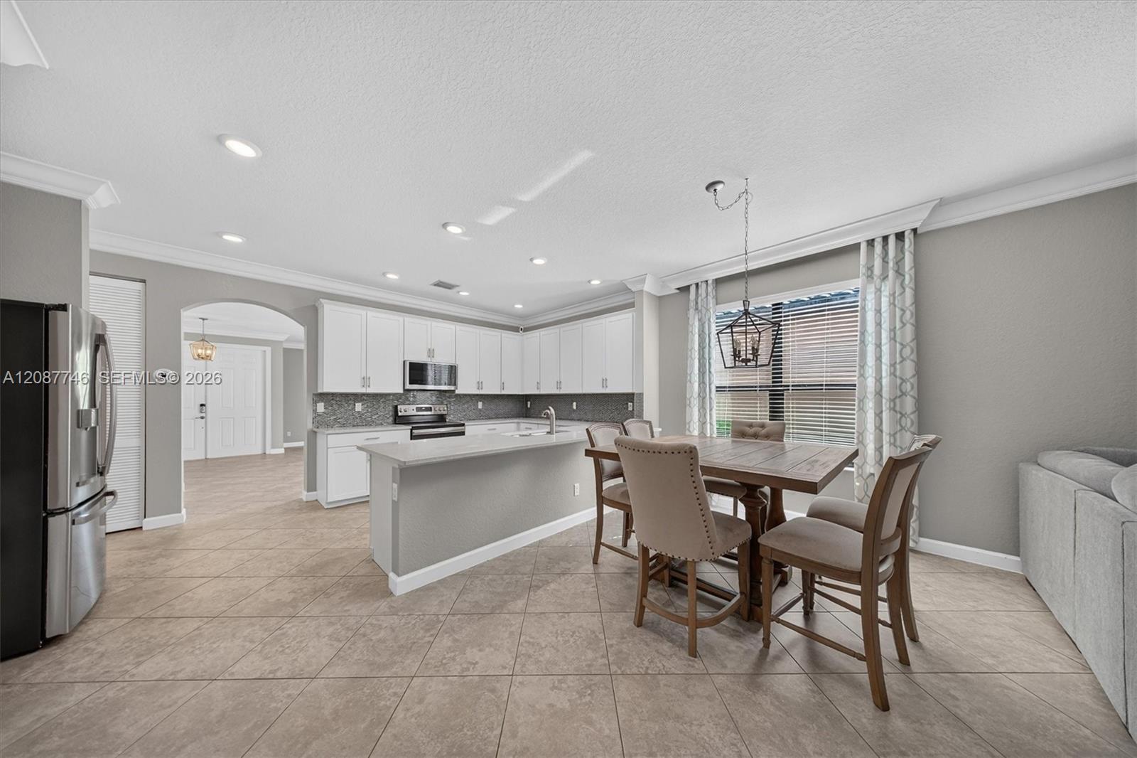 Kitchen and dining area with white cabinets, tiled floors, island, and large window.