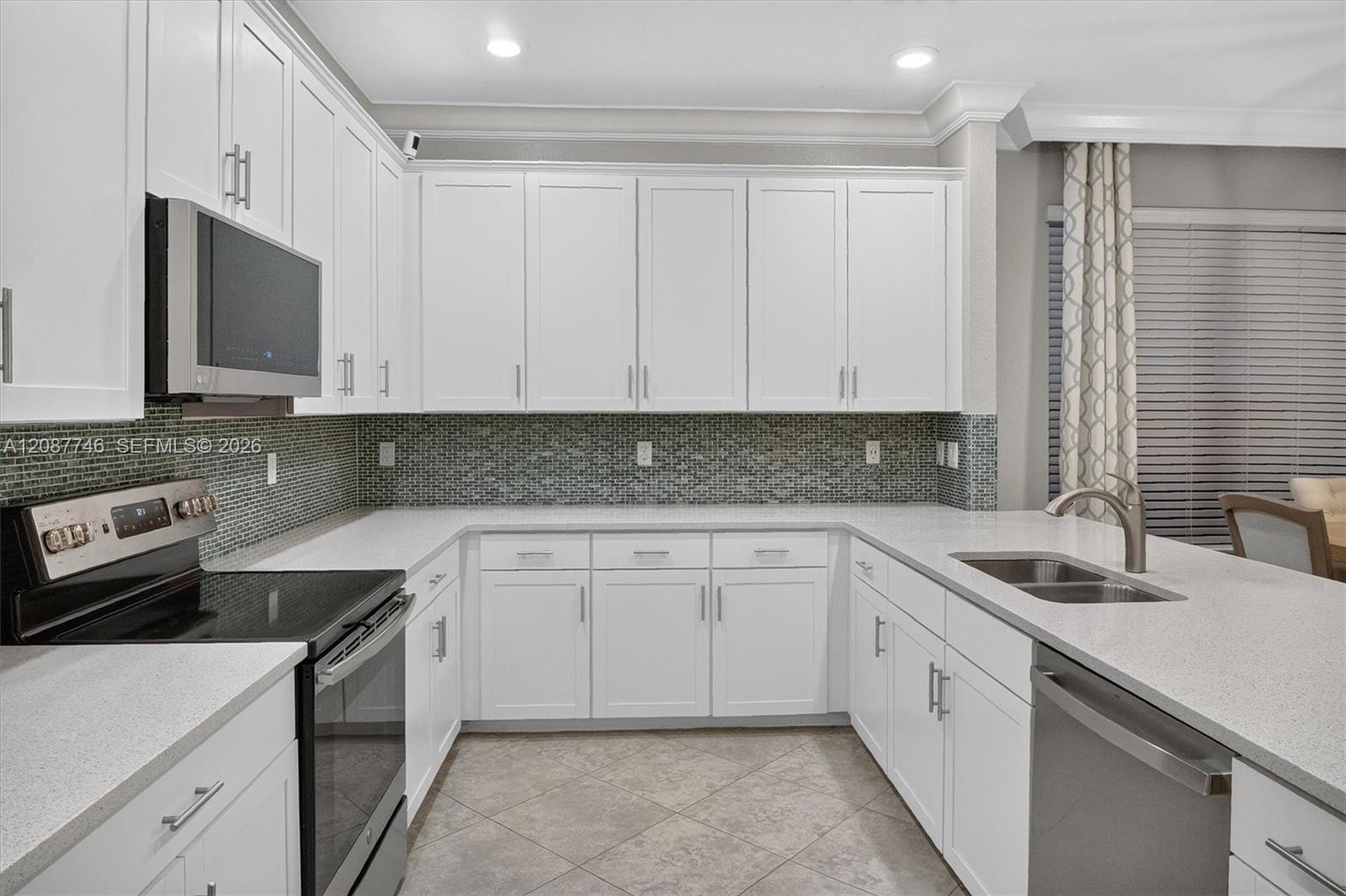 U-shaped kitchen with white cabinets, dark mosaic backsplash, stainless steel appliances, and a double-basin sink.