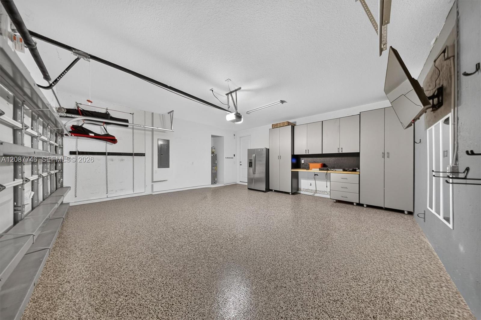 Garage with extensive gray cabinets, wall shelving, overhead storage racks, and a speckled floor.