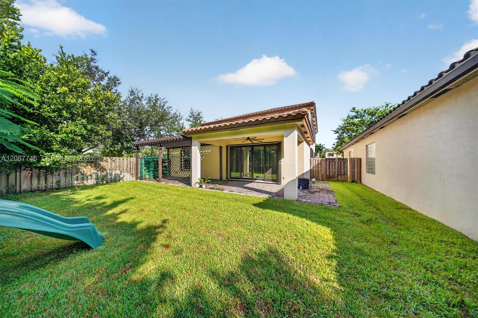Rear of the home with a covered patio, fenced lawn, pergola, and children's slide.