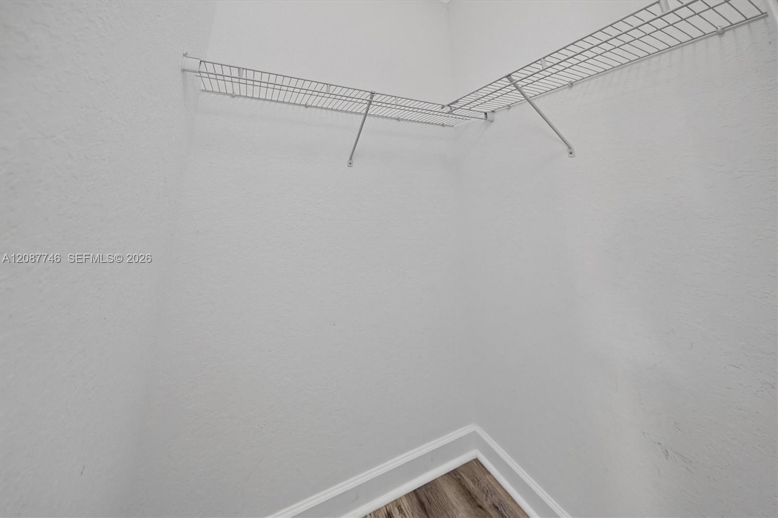 Empty closet with white wire shelving and wood-look flooring.
