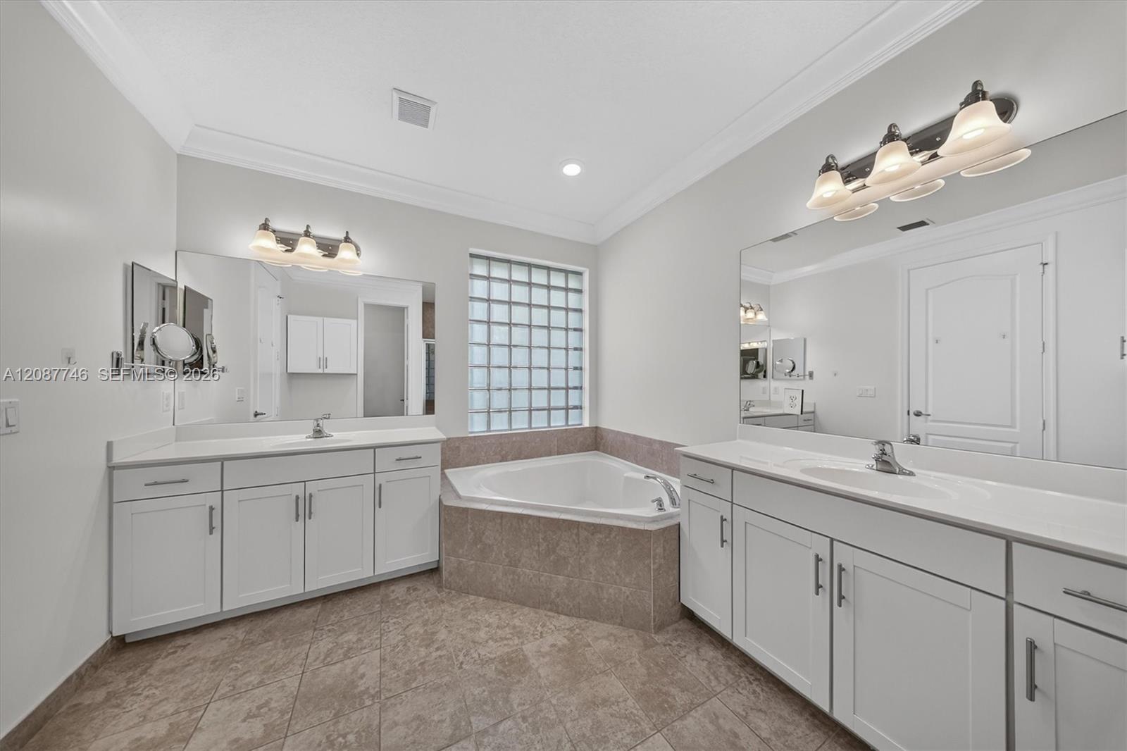 Bathroom with dual white vanities, corner soaking tub, and glass-block window.