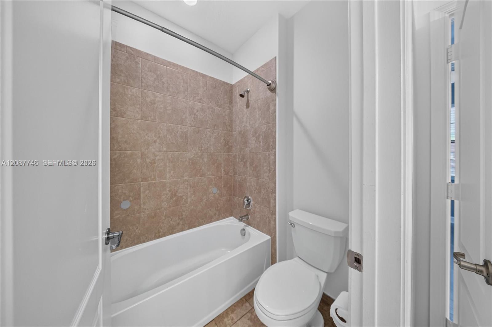 Bathroom with a white bathtub, tan tiled surround, toilet, and narrow window.