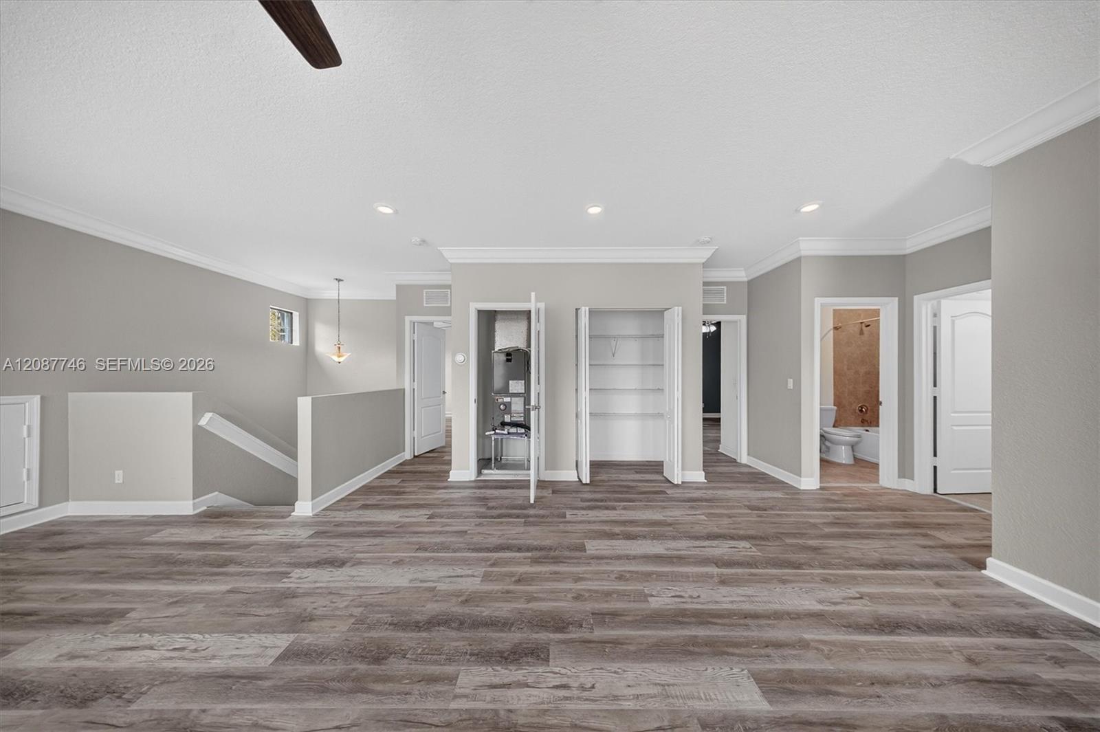 Vacant interior with gray plank flooring, an open stairwell, utility closet, and adjoining bathroom.