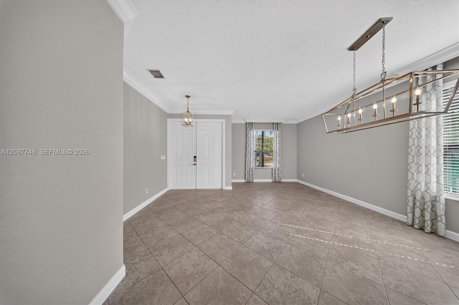 Empty dining room with large tile flooring, a brass-toned chandelier, and curtained windows.