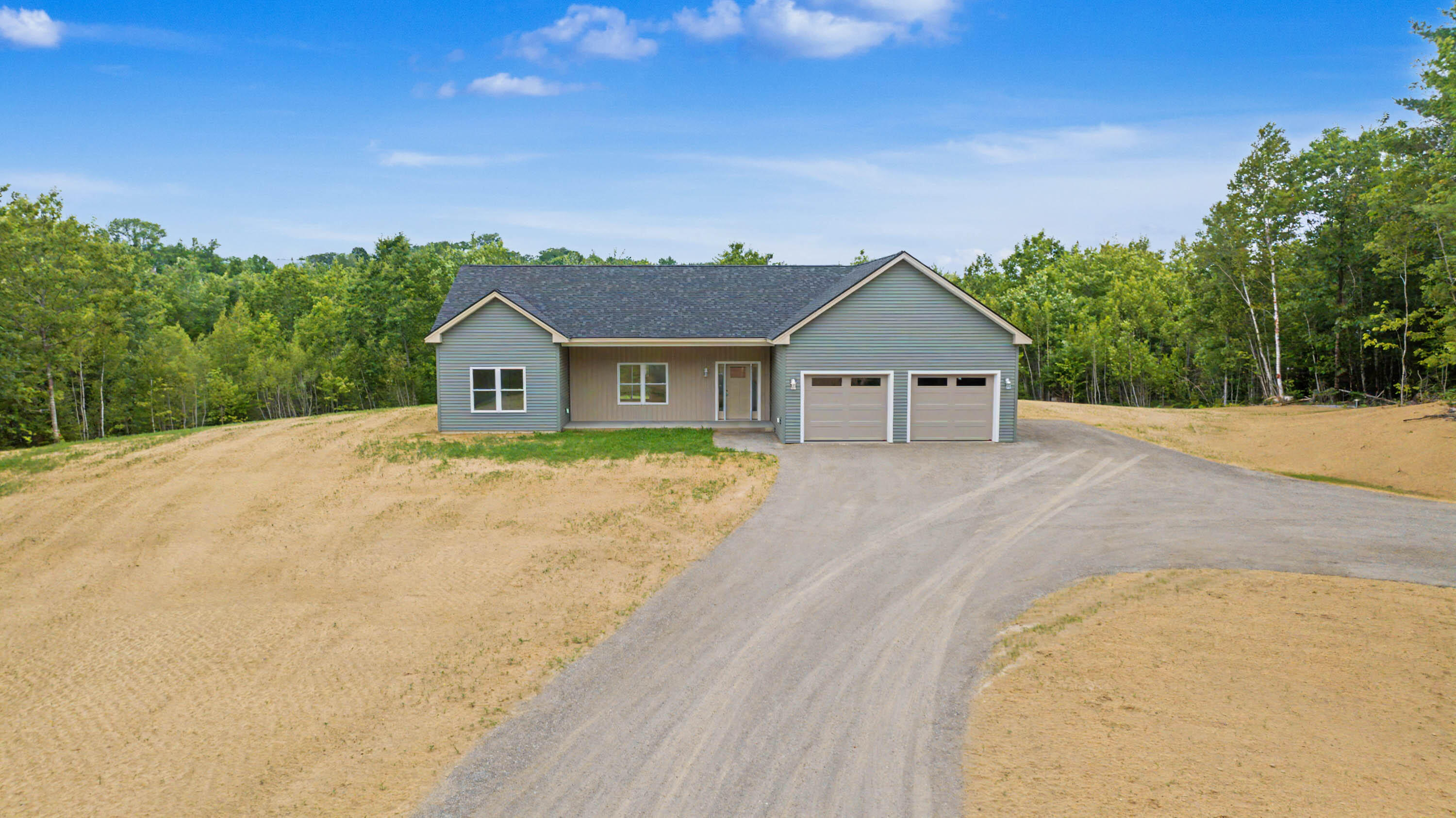Gray single-story home with two garage doors and a curving driveway, surrounded by trees.