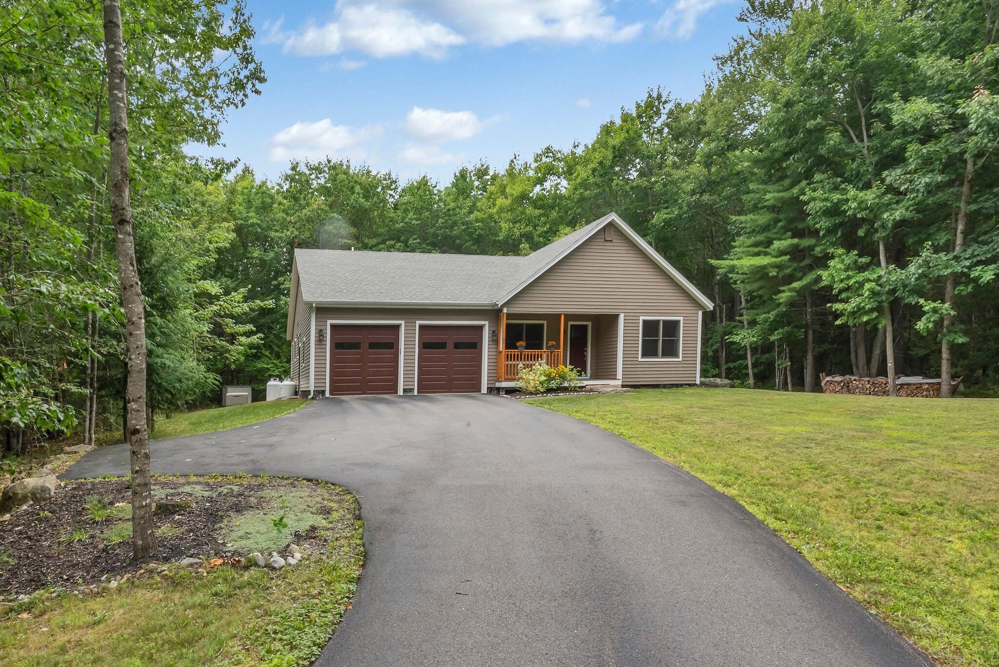 Taupe-sided home with a two-car garage and covered porch, set among trees at the end of a paved driveway.