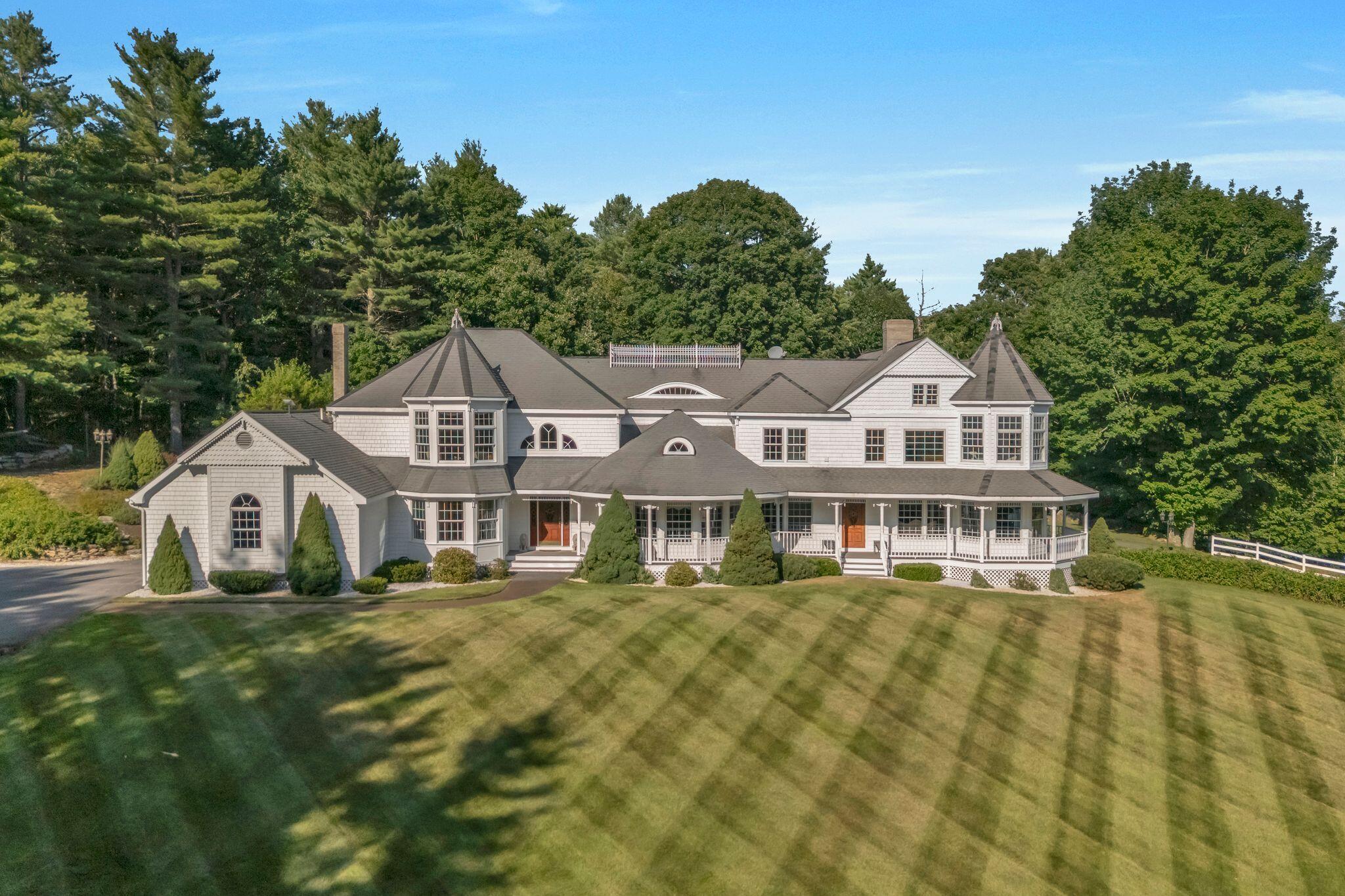 Large white home with turret-like towers and a wraparound porch, surrounded by a broad lawn and mature trees.
