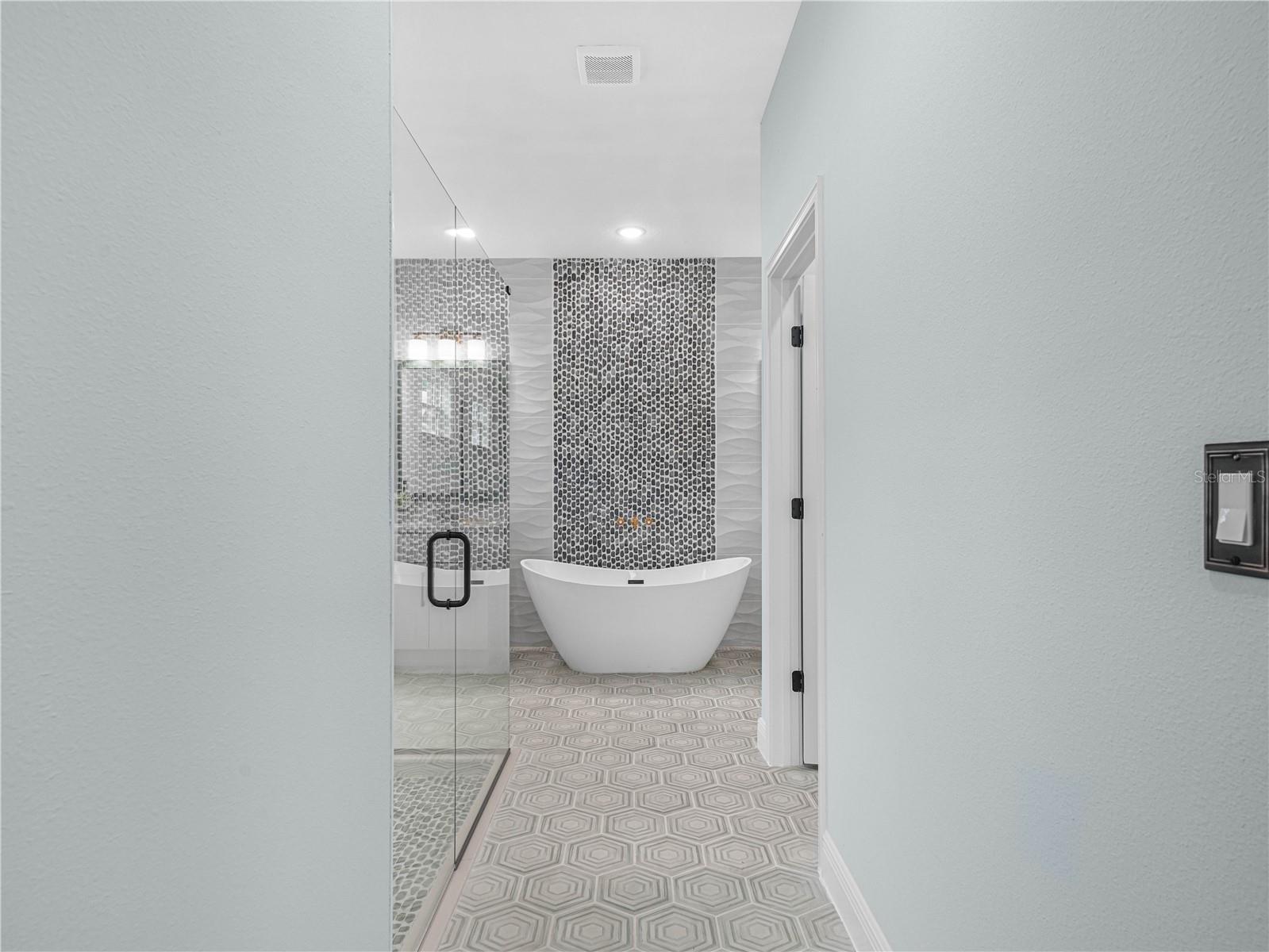 Modern bathroom with a freestanding soaking tub, mosaic accent wall, and glass-enclosed shower.
