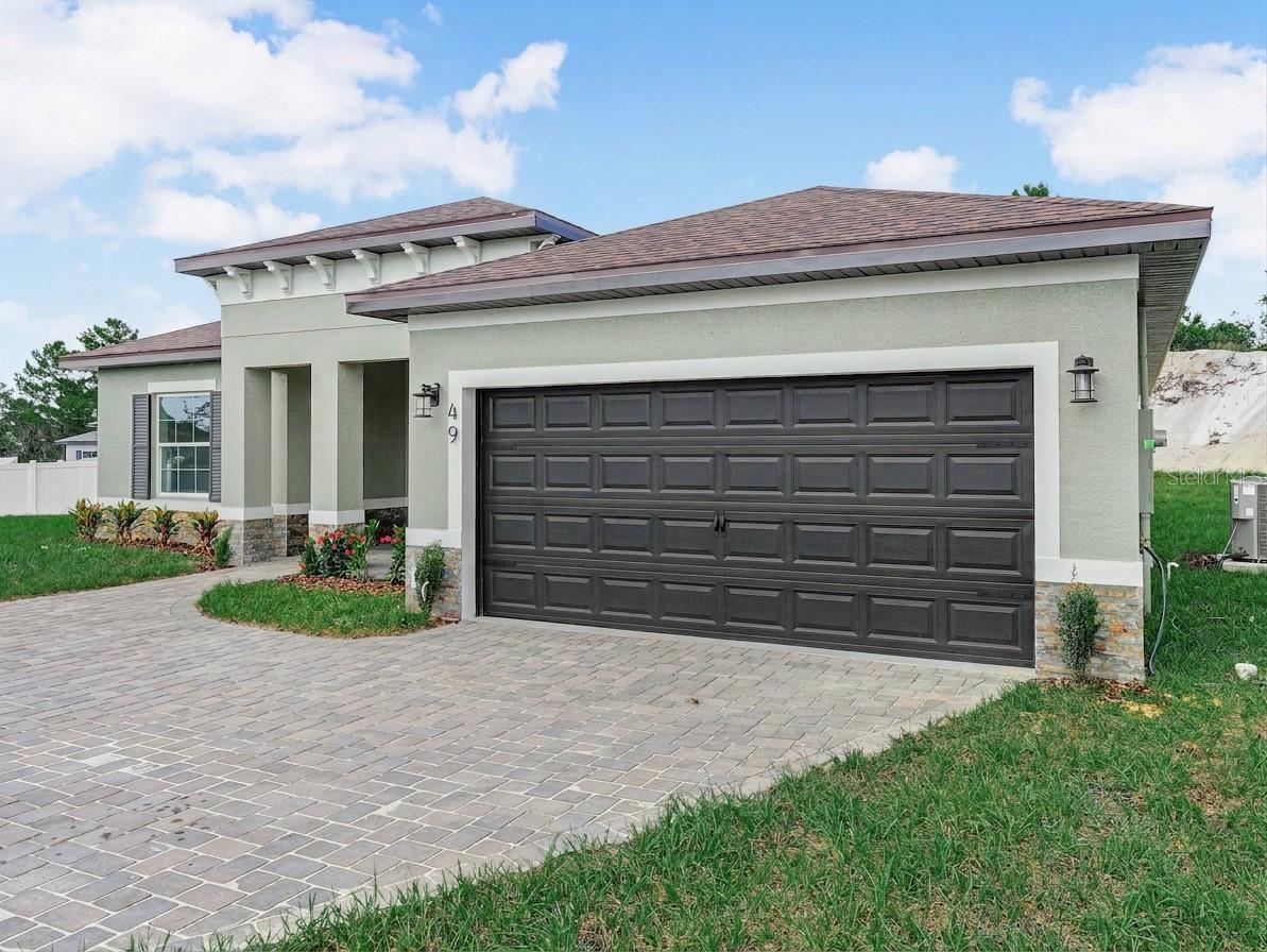 Modern home with a dark double garage door and broad paver driveway.
