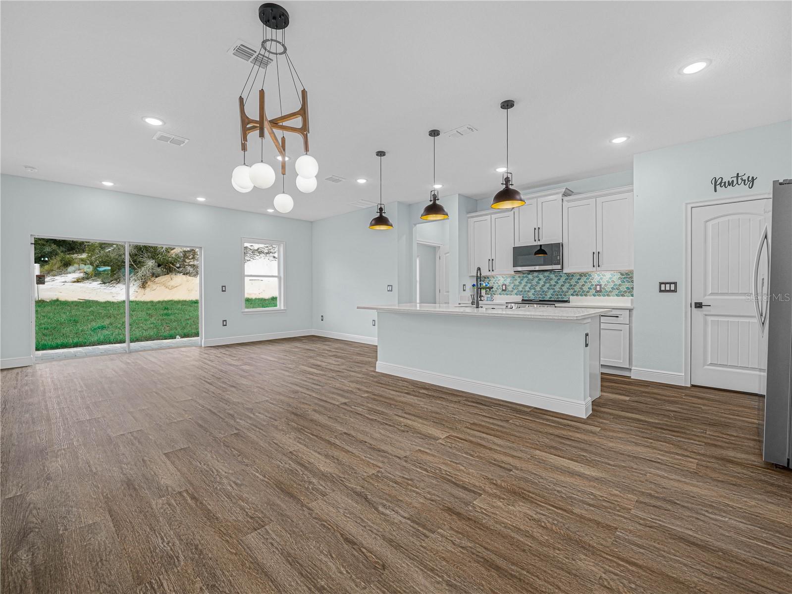 Unfurnished open-plan kitchen with a large island, colorful tile backsplash, and sliding glass doors.