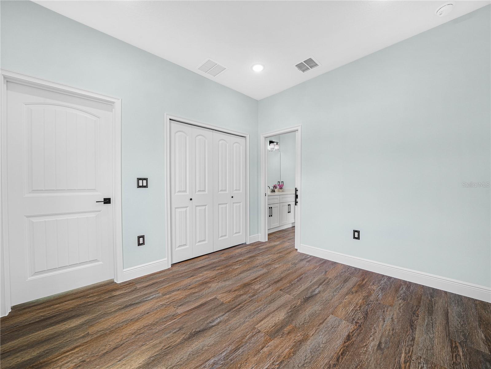 Vacant bedroom with pale blue walls, wood-look flooring, and a double-door closet.