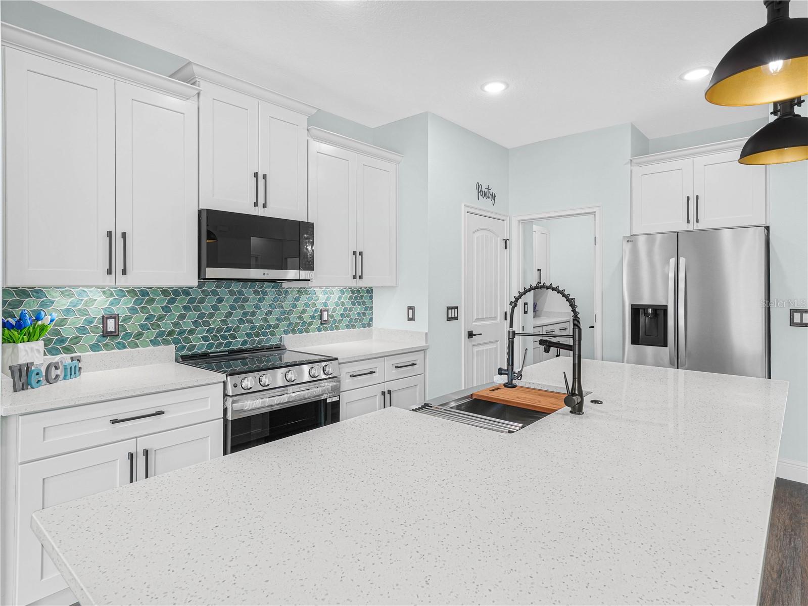 Kitchen with a large white island, teal tile backsplash, white cabinets, and stainless steel appliances.