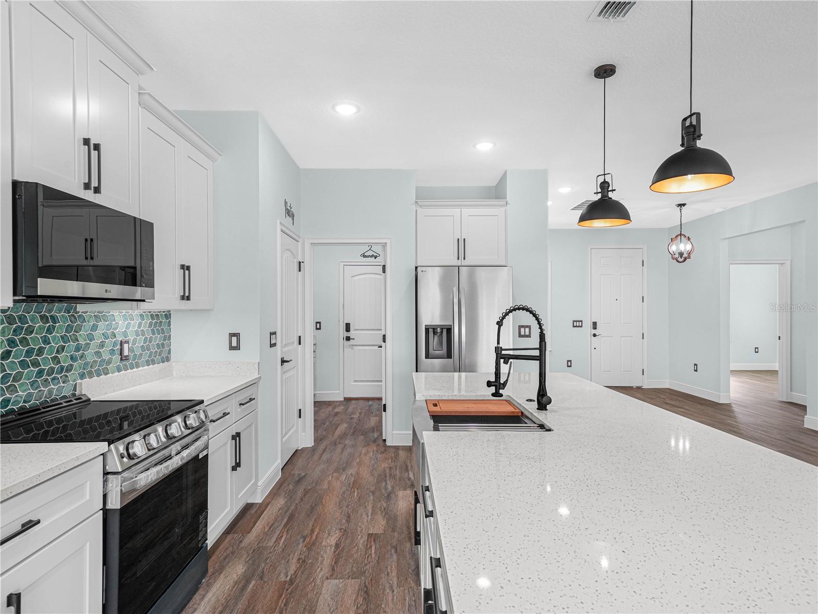 Kitchen with a large quartz island, white cabinetry, stainless appliances, and teal scallop-tile backsplash.