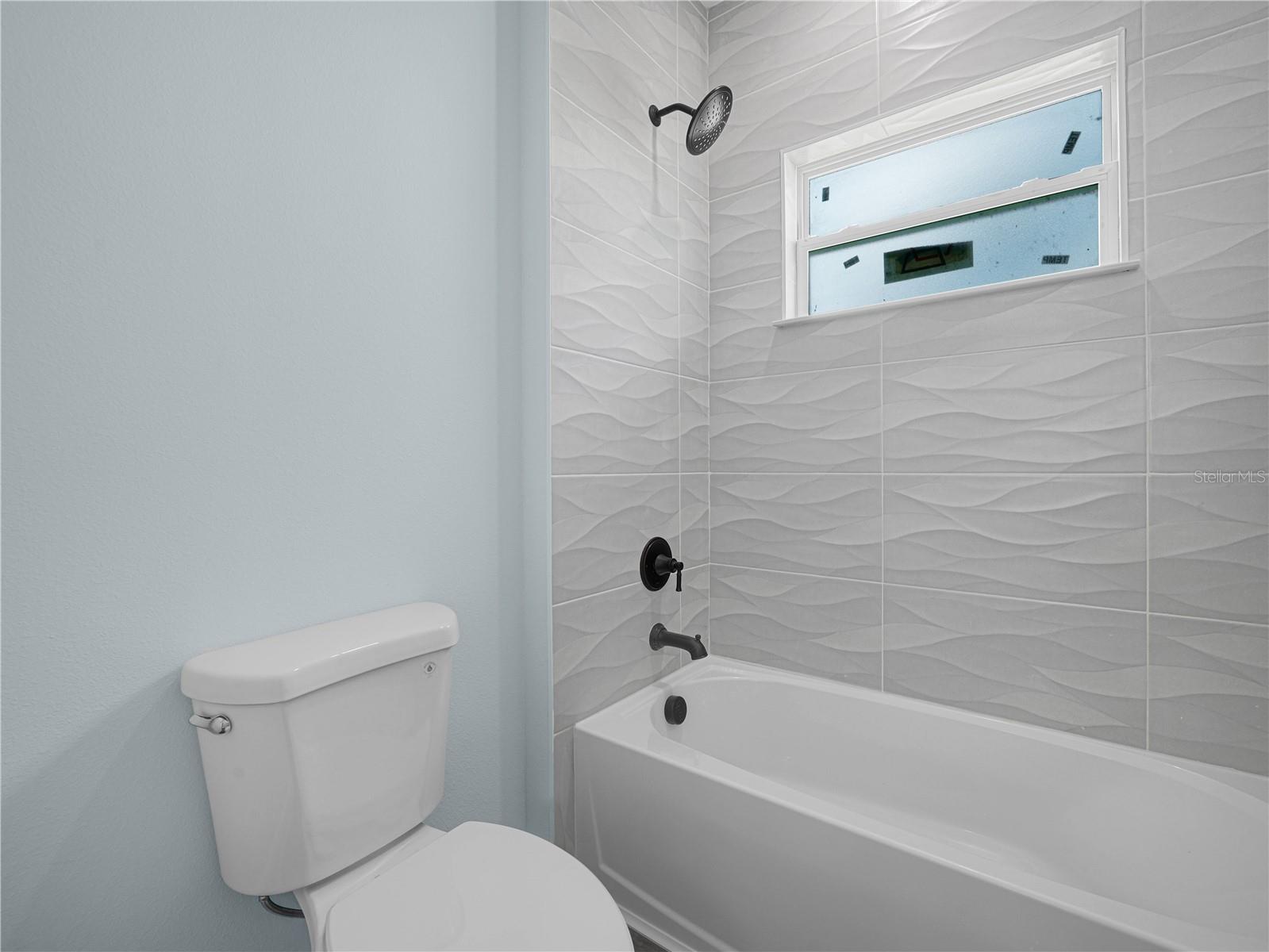 Bathroom with a white tub, wave-pattern tile, black fixtures, and a high frosted window.