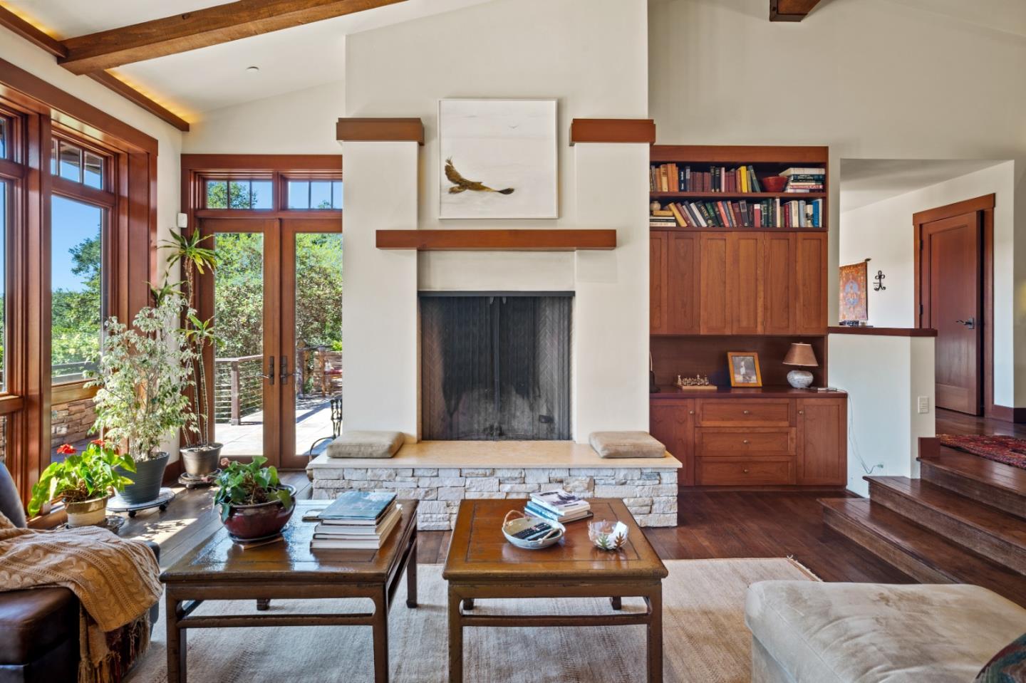 Living room with a stone fireplace, built-in walnut cabinetry, wood beams, and tall patio doors.