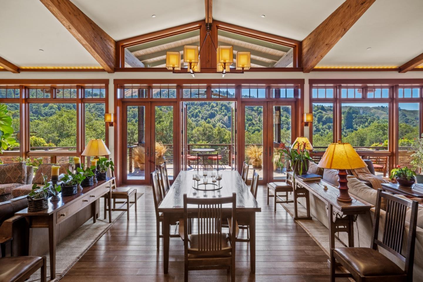 Dining area with exposed timber beams and expansive windows overlooking wooded hills.