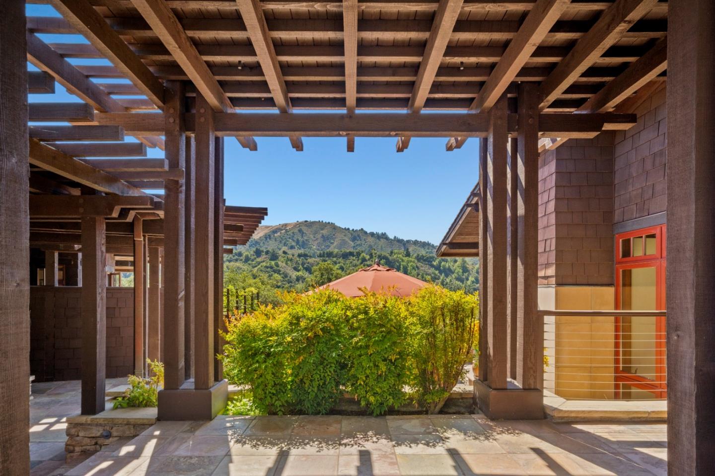 Covered timber patio with stone paving, garden shrubs, and a view of wooded hills.